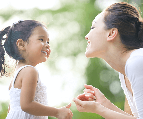 educator smiling outdoors with toddler